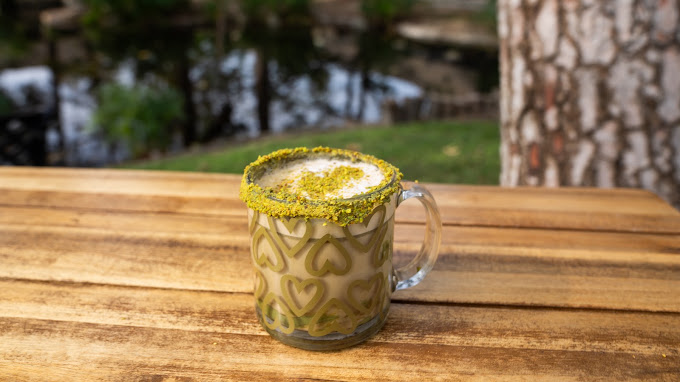A pistachio latte with heart latte art among the trees at dusk